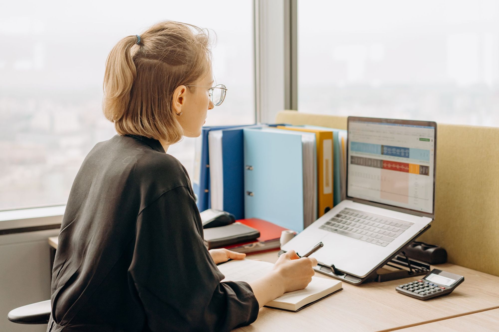 A woman at her desk with a laptop showing a spreadsheet