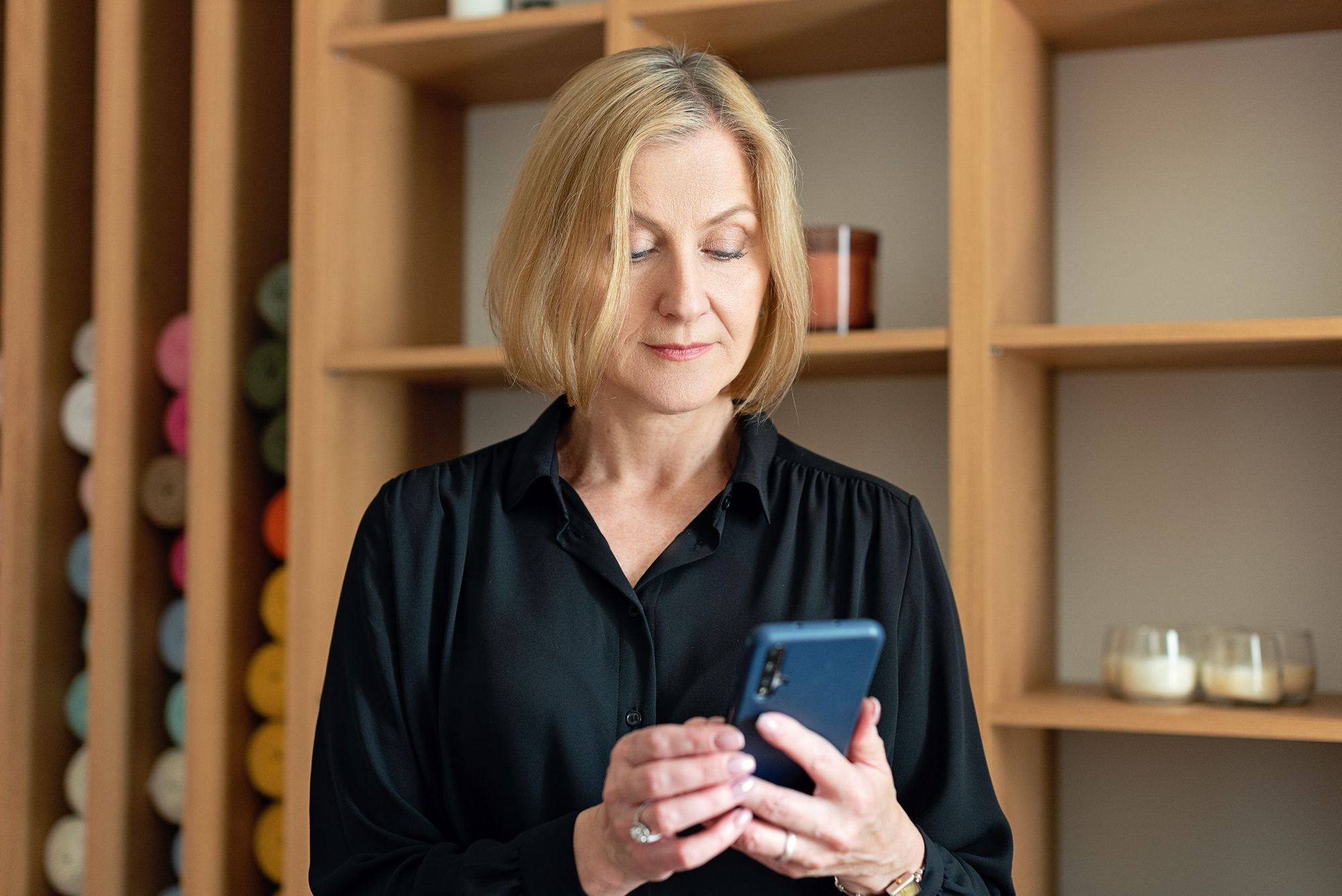 A woman reading her phone in an office with wooden shelves